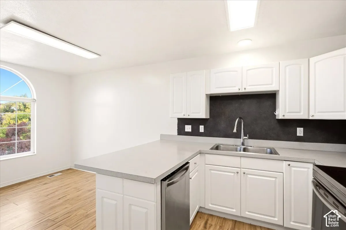 Kitchen featuring white cabinetry, contrasting dark backsplash, stainless steel sink with high-arc faucet, solid-surface countertops, and wood-finish flooring