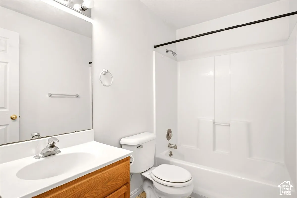 Bathroom featuring a vanity with a white integrated sink, wood-finish cabinetry, a full-width mirror, and a shower-tub combination with a molded surround