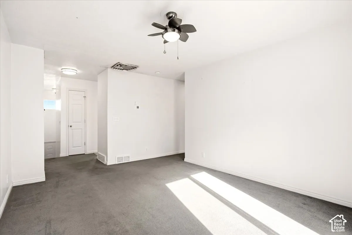 Neutral-toned wall-to-wall carpeting, multi-blade ceiling fan with integrated lighting, and a solid-core interior door