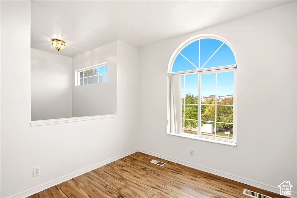 Room featuring wood-finish flooring, an arched window, a secondary rectangular window opening, and a flush-mount light fixture