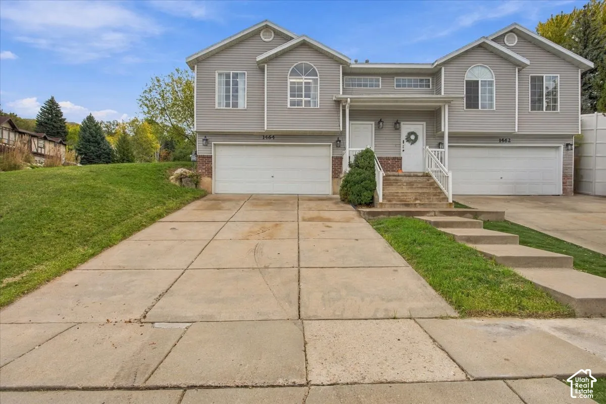 Multi-level exterior featuring light gray horizontal siding, brick masonry detailing, dual two-car garages, arched windows, and concrete driveways