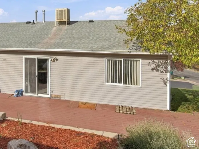 Single-story residence featuring light gray horizontal siding, an expansive ground-level composite deck, two sets of sliding glass doors, and mature landscaping