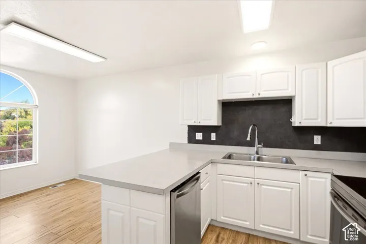 Kitchen featuring white cabinetry, contrasting dark backsplash, stainless steel sink with high-arc faucet, solid-surface countertops, and wood-finish flooring