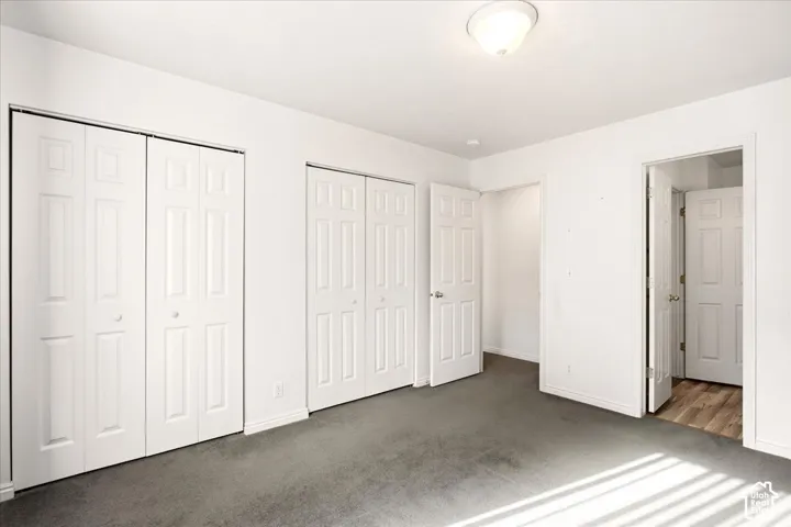 Interior room featuring neutral wall-to-wall carpeting, two sets of white paneled bi-fold closet doors, a classic white interior door, and a flush-mount ceiling fixture