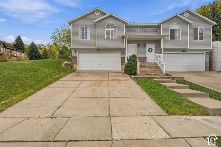 Multi-level exterior featuring light gray horizontal siding, brick masonry detailing, dual two-car garages, arched windows, and concrete driveways