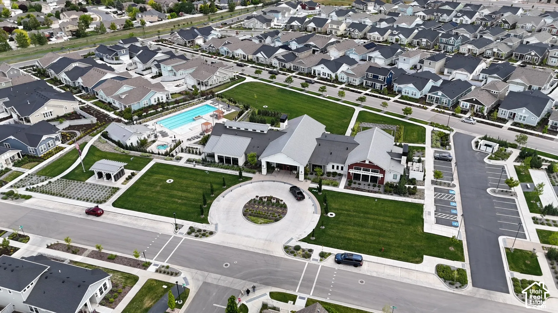 Aerial perspective of community facilities featuring an outdoor swimming pool, spa, circular driveway, landscaped lawn, and dedicated parking area