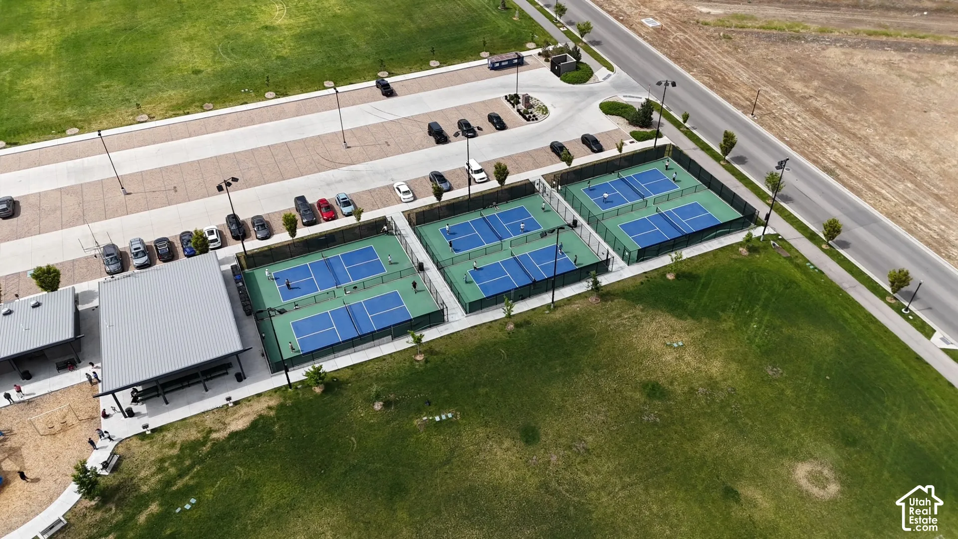 Recreational area featuring four fenced pickleball courts, an open-air pavilion with metal roofing, and expansive green space