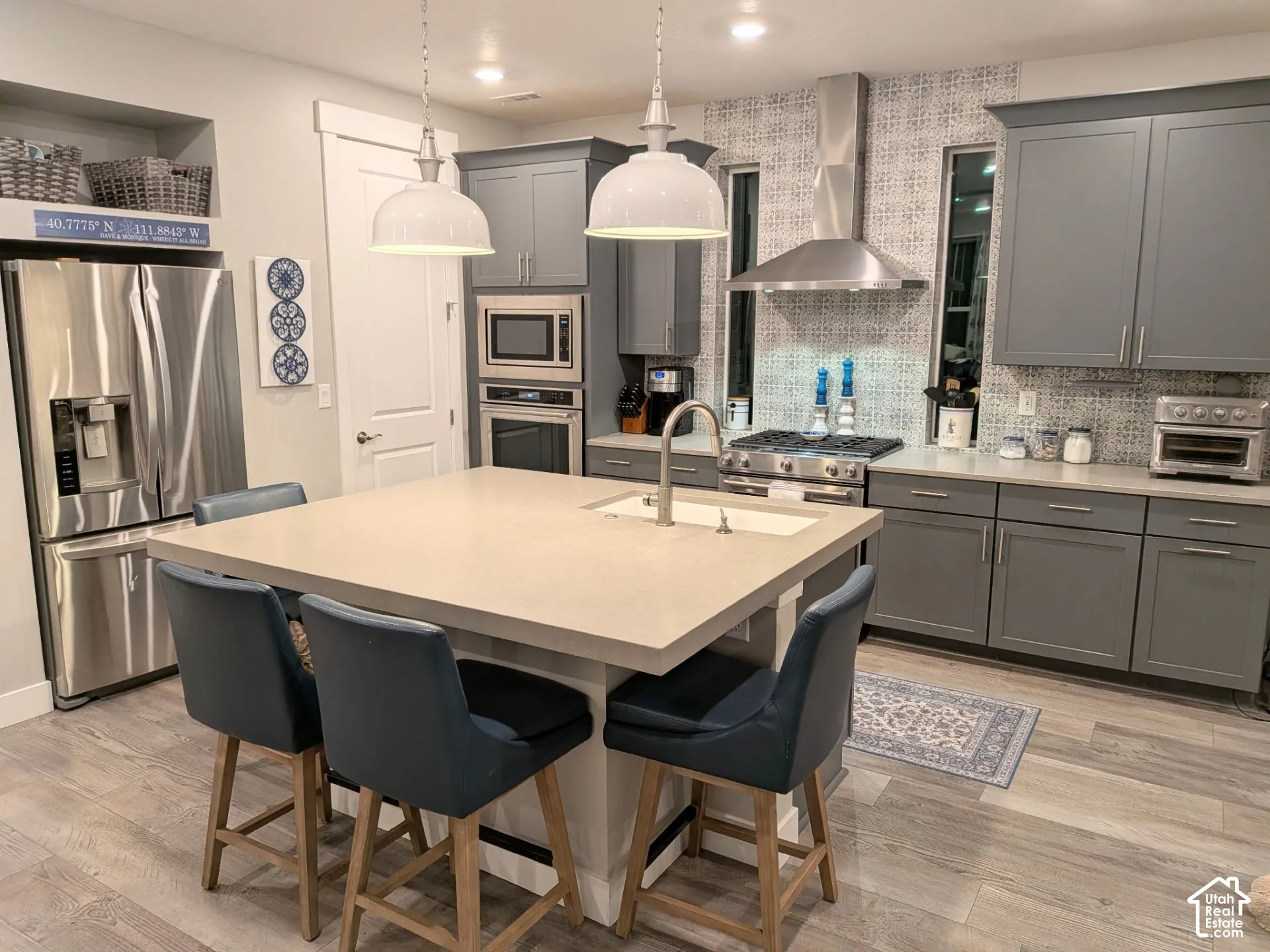 Kitchen featuring gray cabinetry, a central island with a solid-surface countertop, stainless steel appliances, a patterned tile backsplash, and wood-finish flooring