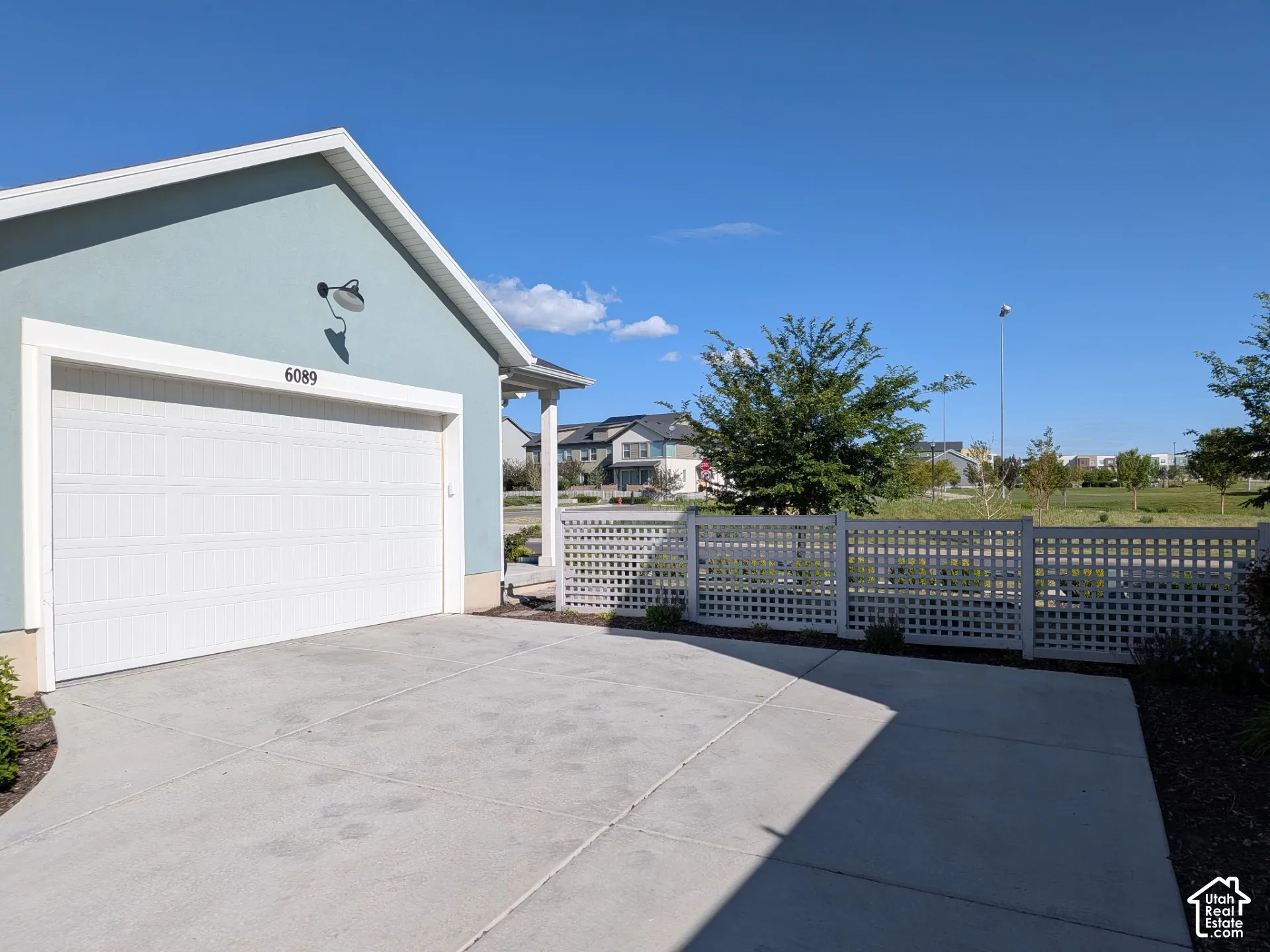 Light blue exterior with a white garage door, concrete driveway, and white lattice fencing