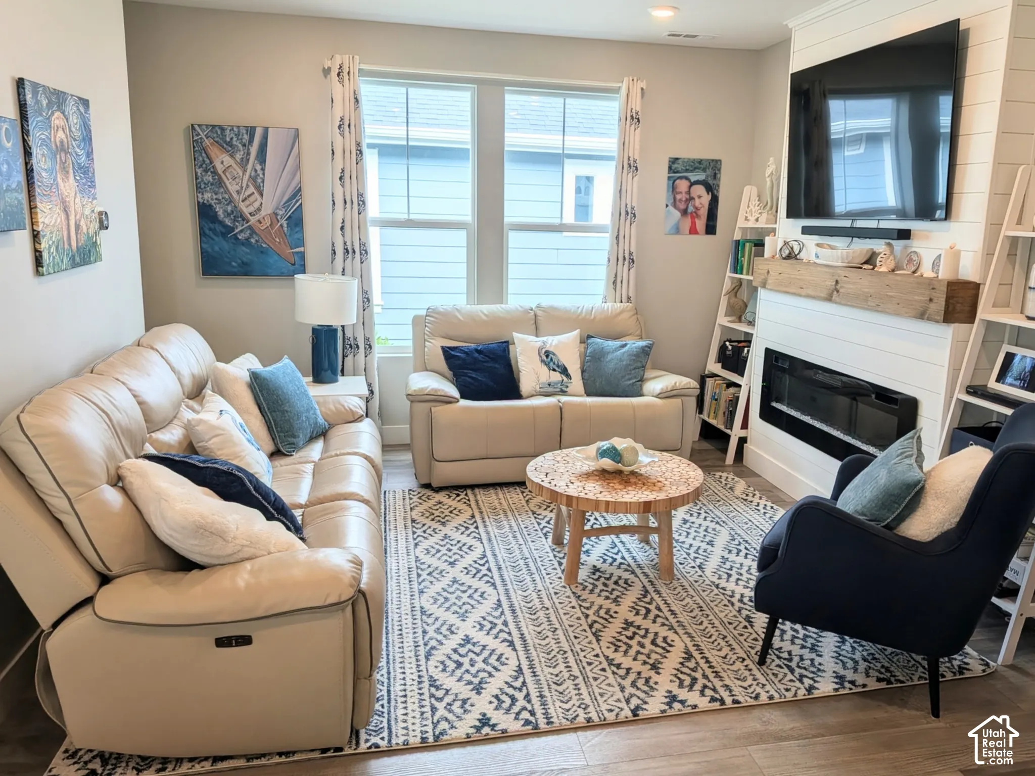 Living area featuring an electric fireplace with white horizontal shiplap surround, wood-finish mantel, wood-finish flooring, and dual double-pane windows