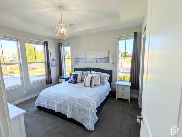 Tray ceiling with a decorative chandelier, expansive windows, and wall-to-wall carpeting
