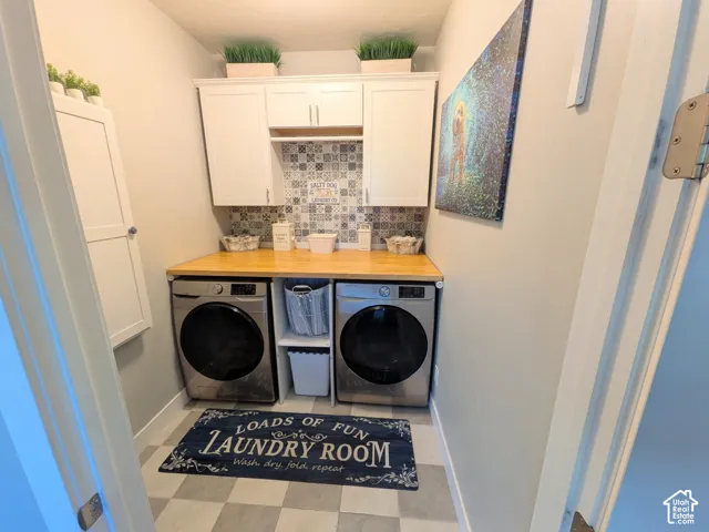 Laundry area featuring white shaker-style wall cabinetry, patterned tile backsplash, wood-surface countertop, and built-in center shelving