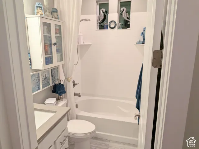 Bathroom featuring a white vanity with a neutral solid-surface countertop, built-in upper cabinetry with glass-panel doors, a soaking tub with an integrated shower, and vertical transom windows