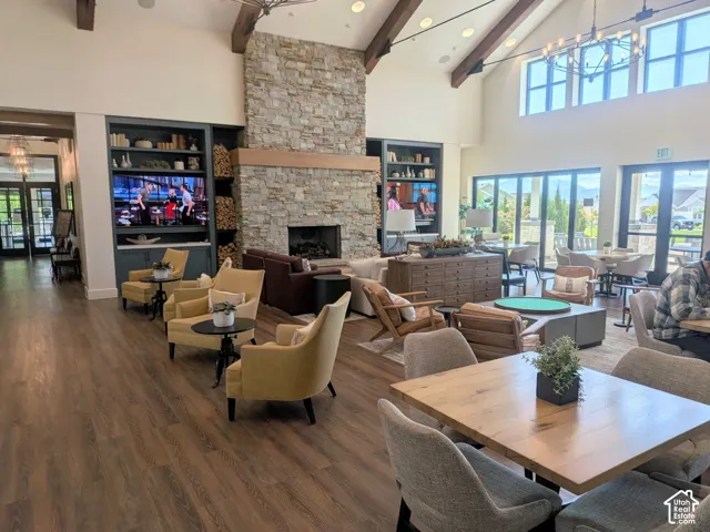 Vaulted ceilings with exposed timber beams, floor-to-ceiling stone masonry fireplace, wood-finish flooring, built-in cabinetry with integrated shelving, and large multi-pane windows