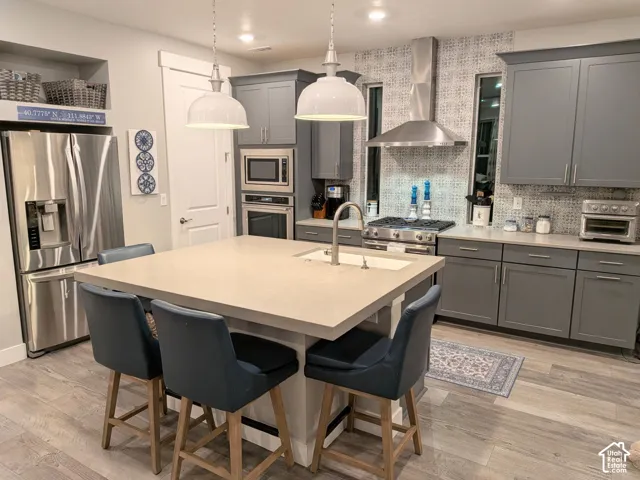 Kitchen featuring gray cabinetry, a central island with a solid-surface countertop, stainless steel appliances, a patterned tile backsplash, and wood-finish flooring