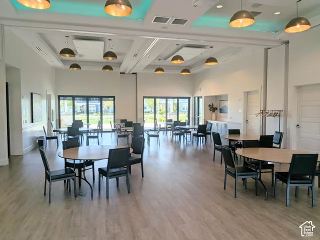 Expansive multi-purpose hall featuring coffered ceilings with integrated recessed lighting, pendant light fixtures, wood-finish flooring, and floor-to-ceiling multi-panel glass doors