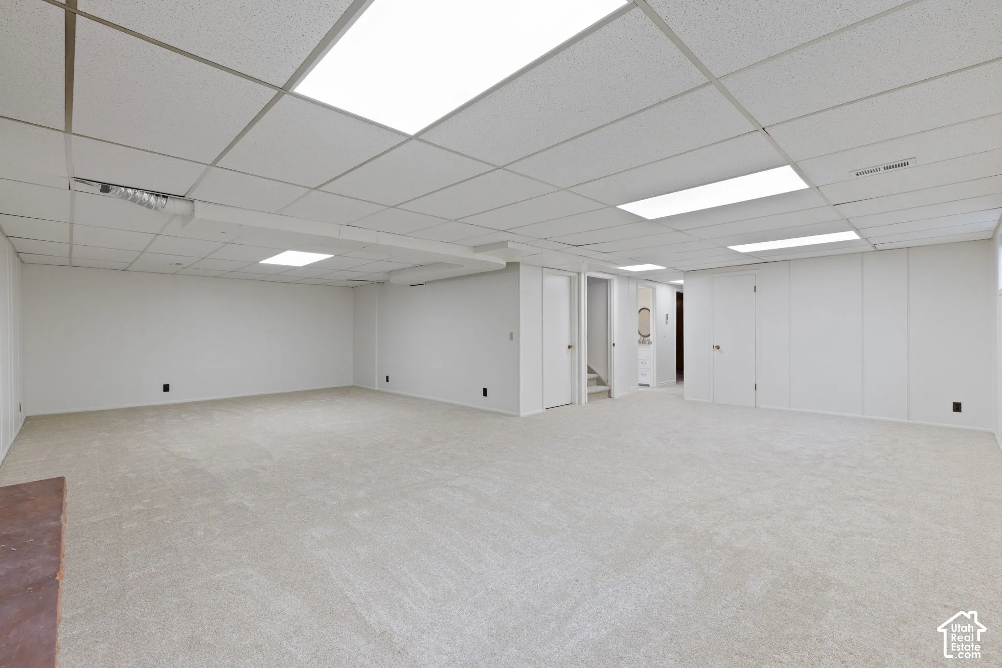 Expansive interior space featuring neutral wall-to-wall carpeting, white paneled walls, and recessed fluorescent lighting with a drop ceiling