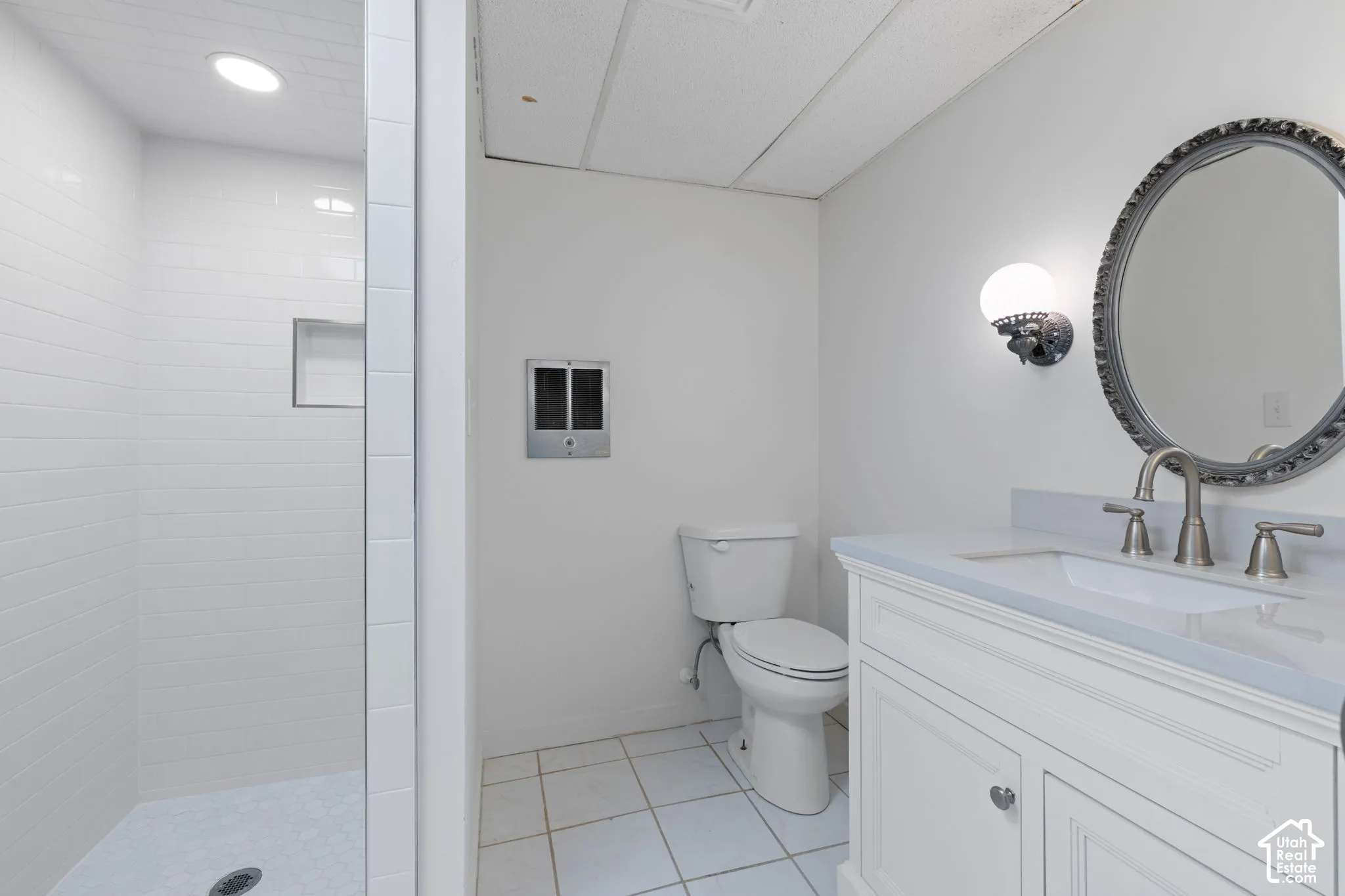 Bathroom featuring a white vanity with a composite countertop and undermount sink, walk-in shower with tiled walls and an integrated niche, and circular wall-mounted mirror