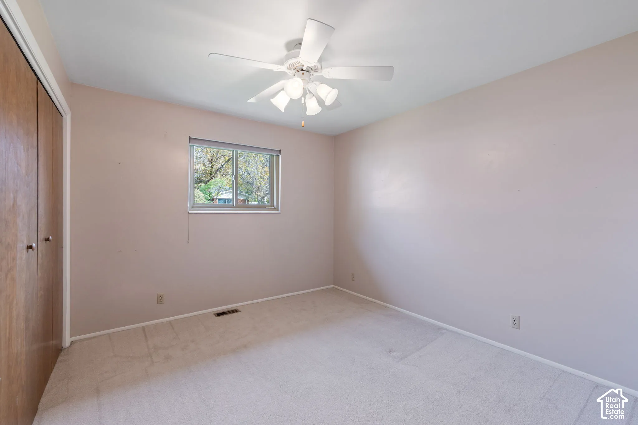 Room featuring carpeted flooring, a ceiling fan with integrated lighting, a single window, and wooden-finish closet doors