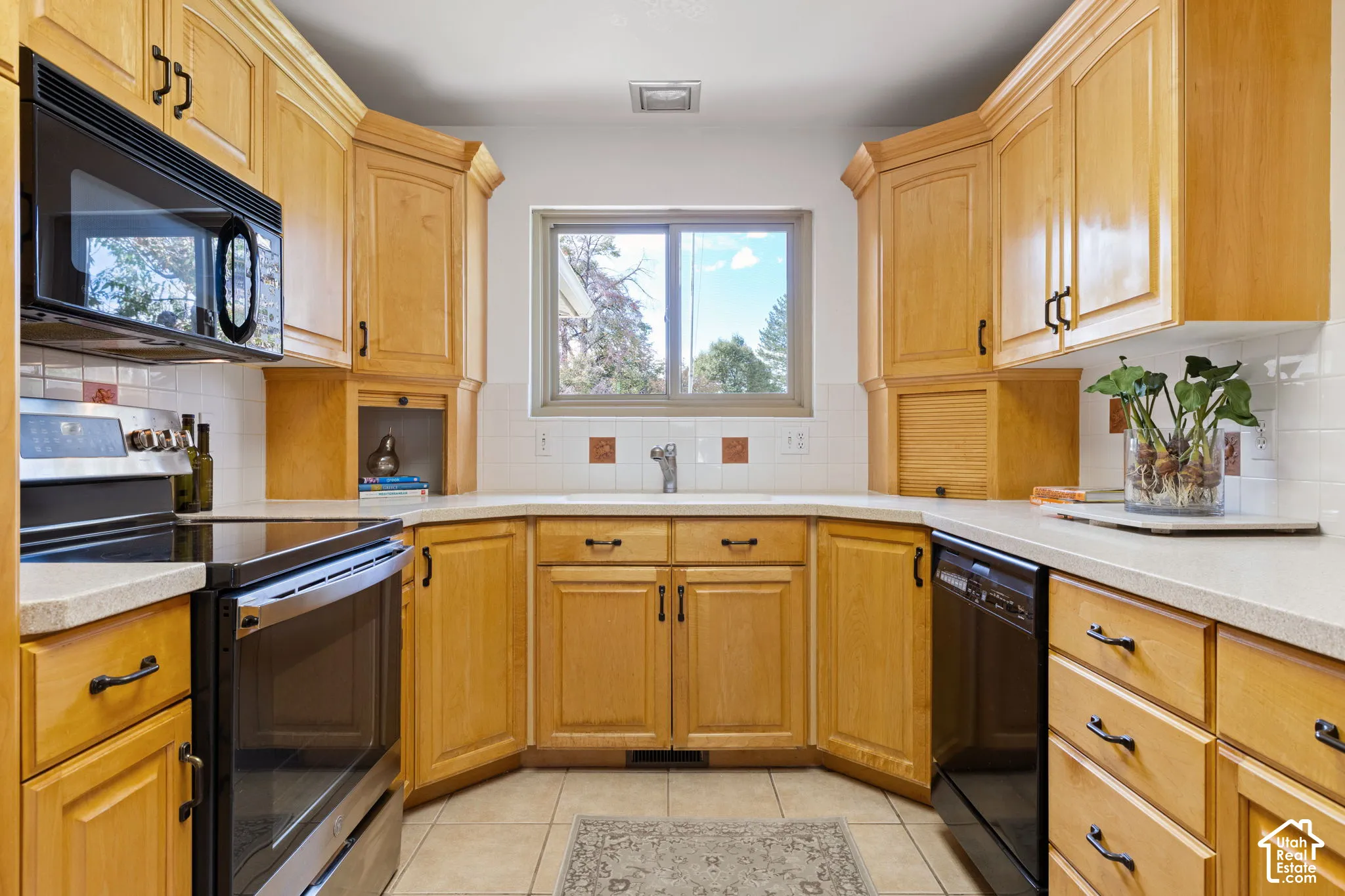 Kitchen featuring light-finish cabinetry, neutral solid-surface countertops, white tile backsplash, black appliance package, and tile flooring