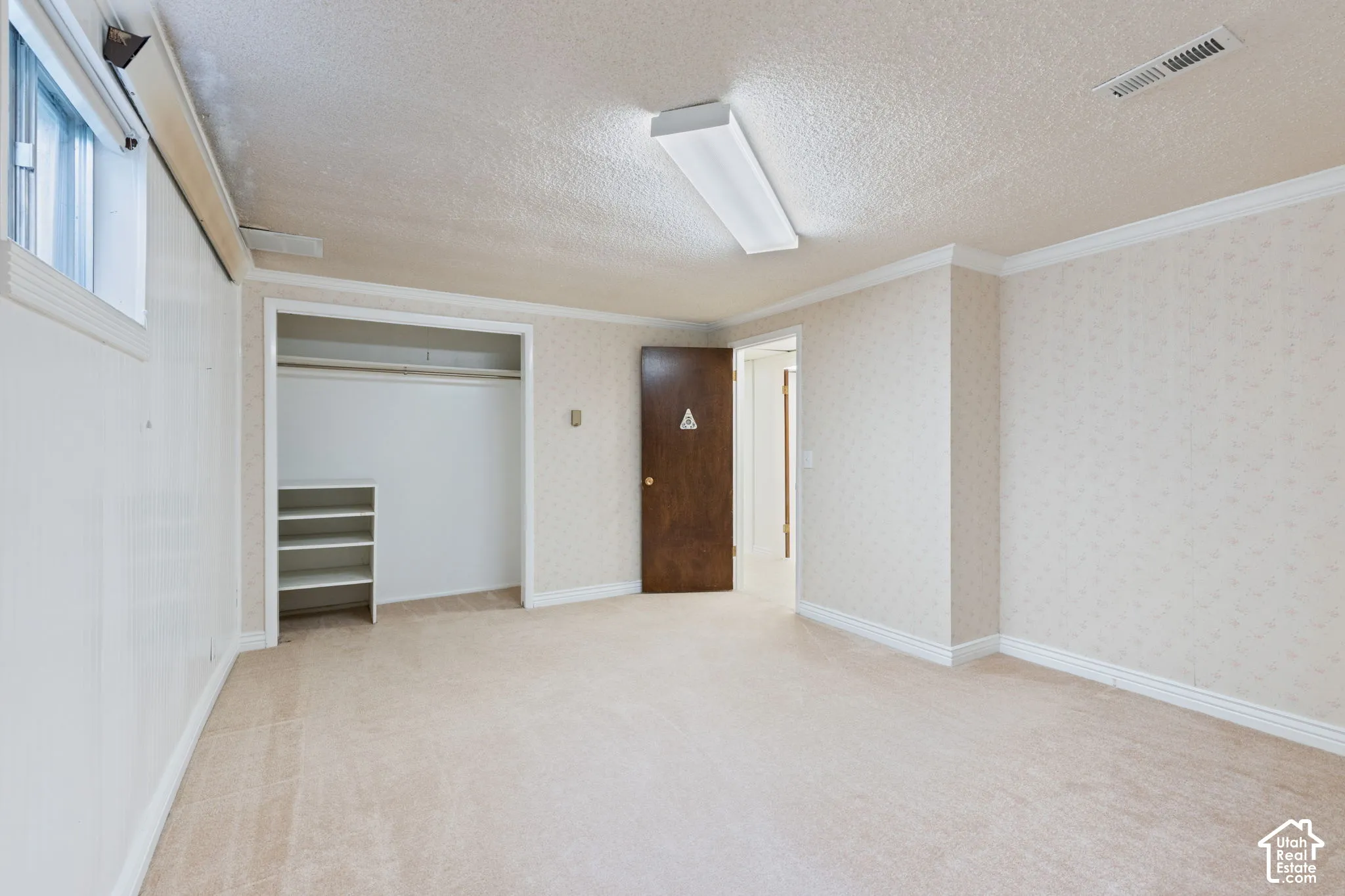 Room featuring wall-to-wall carpeting, textured ceiling, crown molding, and a built-in closet with integrated shelving