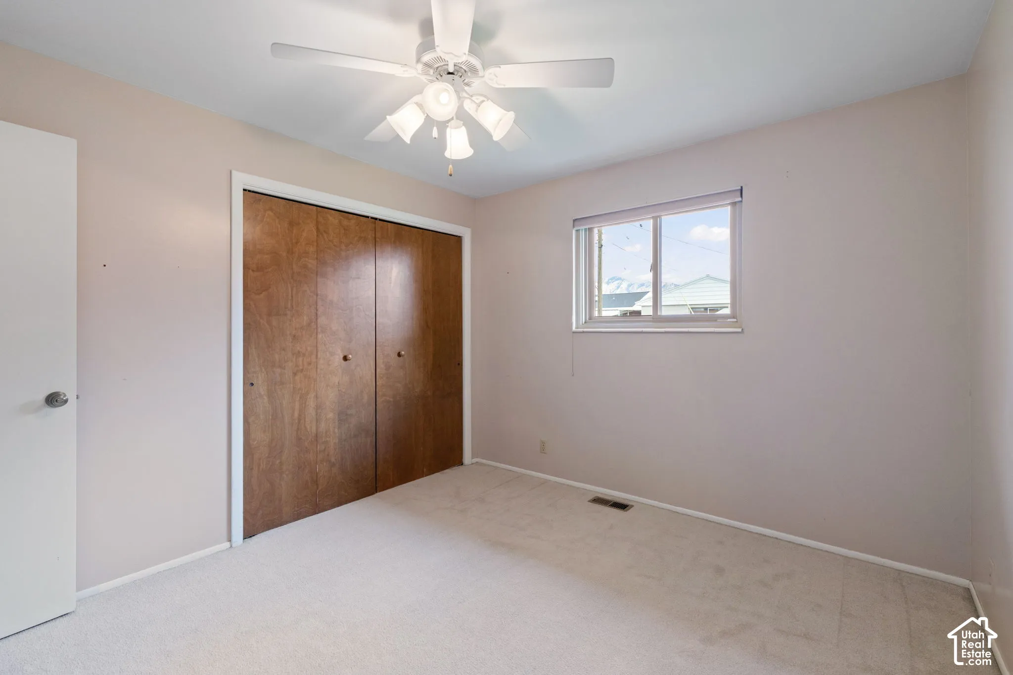 Neutral wall tones paired with light carpeting, a sliding dual-panel closet with wood-finish doors, a multi-light ceiling fan, and a horizontal sliding window