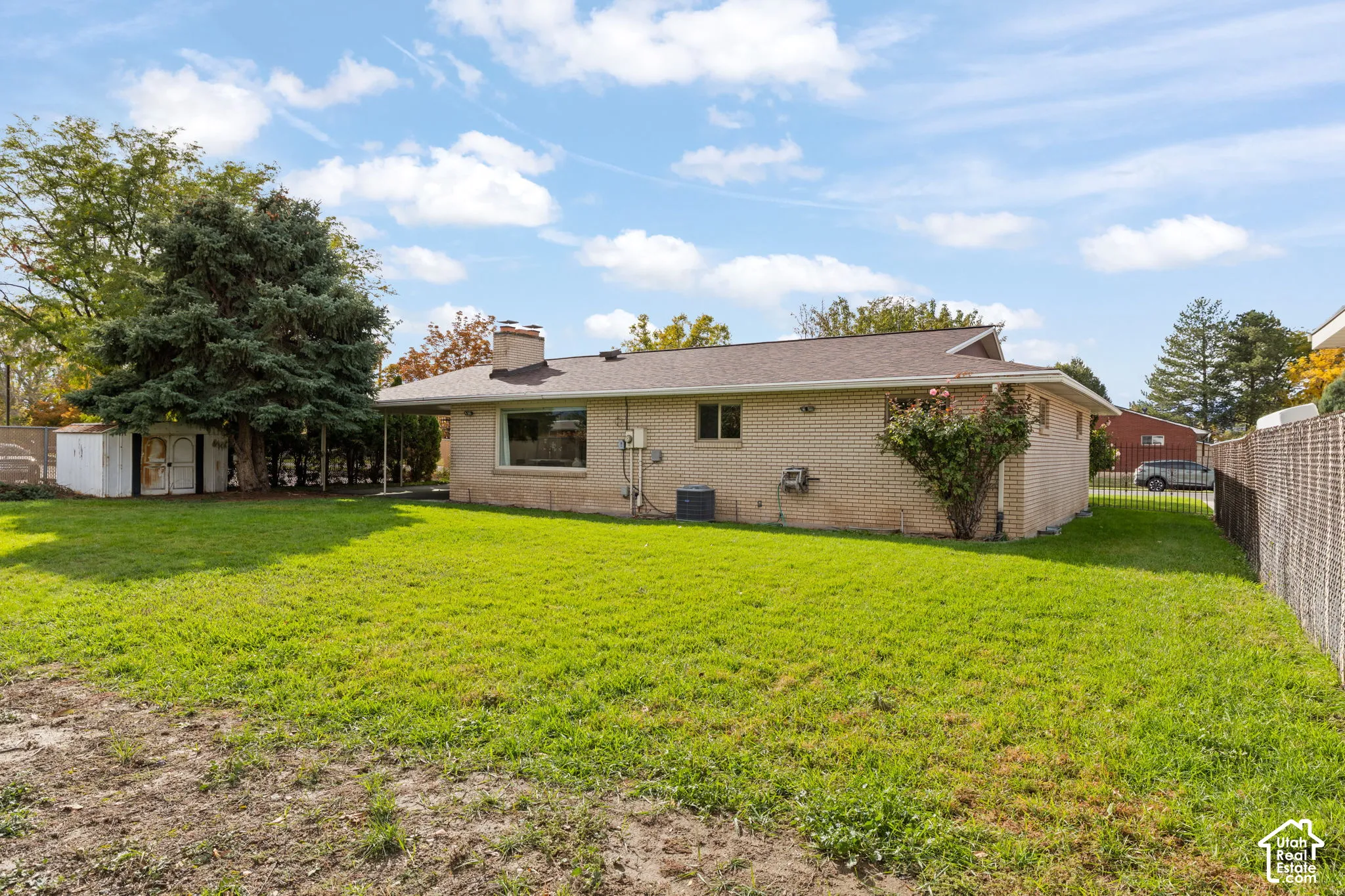Brick exterior featuring a rear-facing chimney, covered patio, mature landscaping, and an attached storage shed