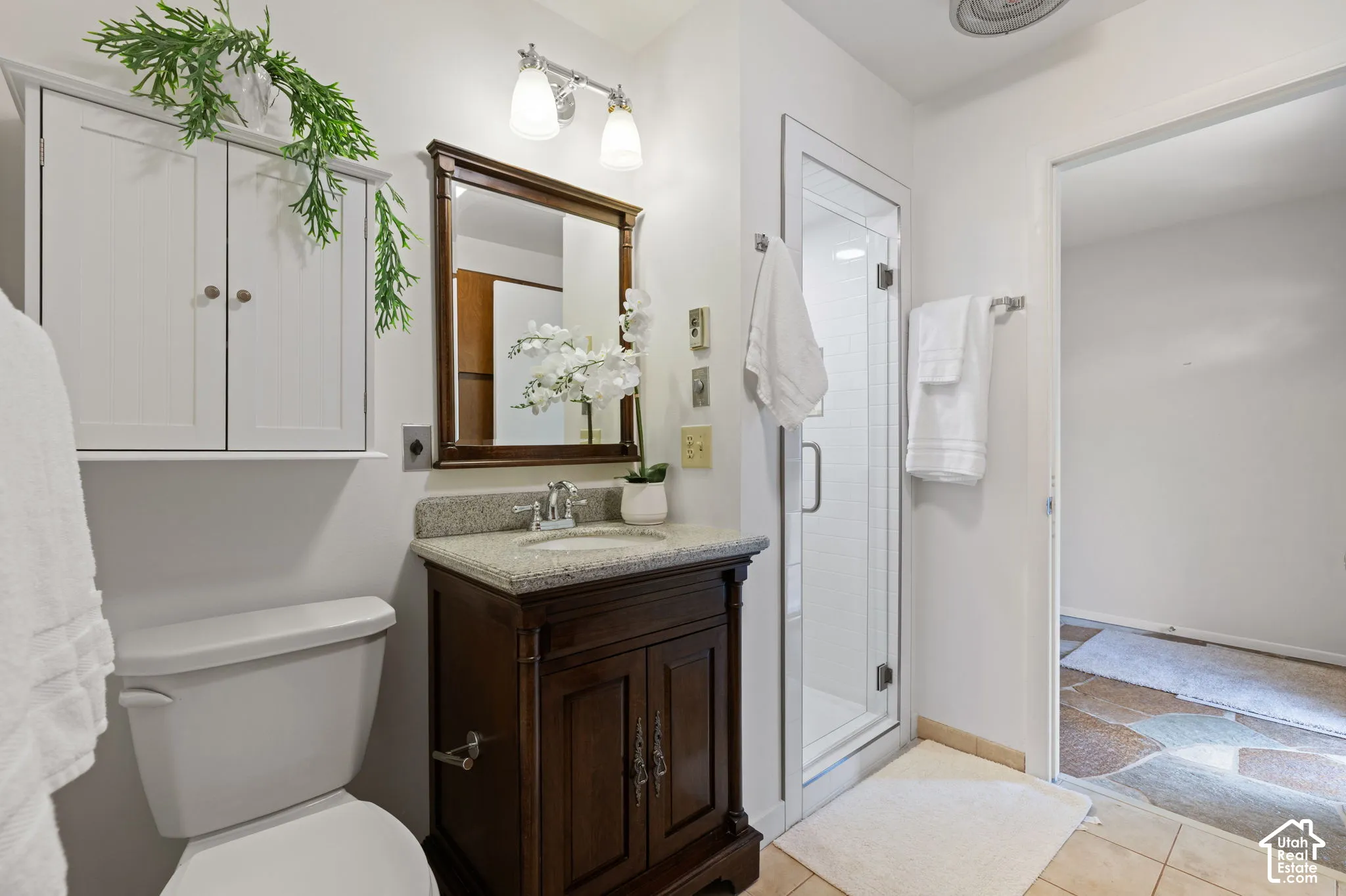 Bathroom featuring a dark wood-finish vanity with a stone countertop, an integrated sink, a wall-mounted medicine cabinet, and a glass-enclosed shower