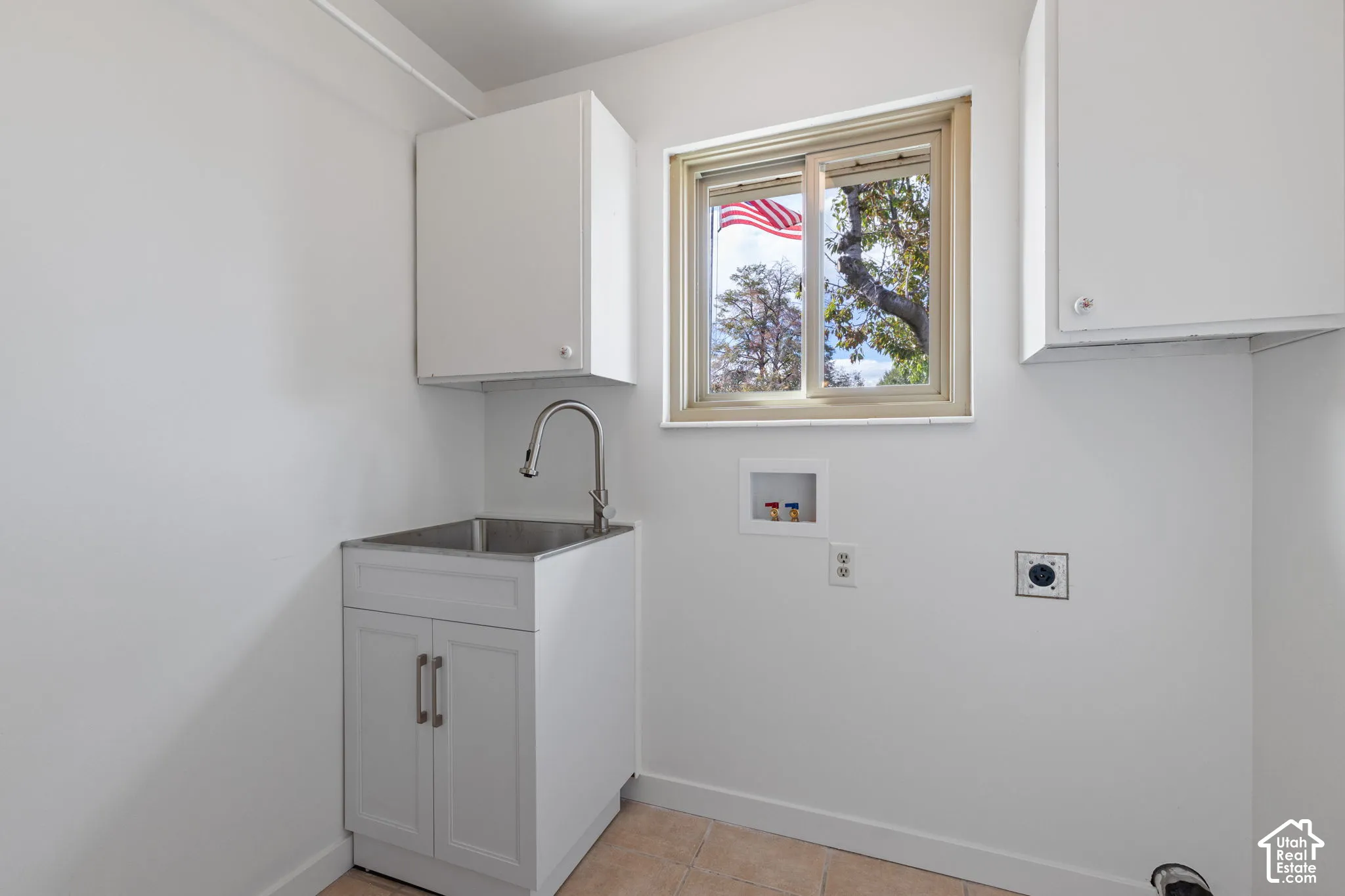 Laundry area featuring white cabinetry, stainless steel basin sink with gooseneck faucet, tile flooring, and integrated utility hookups