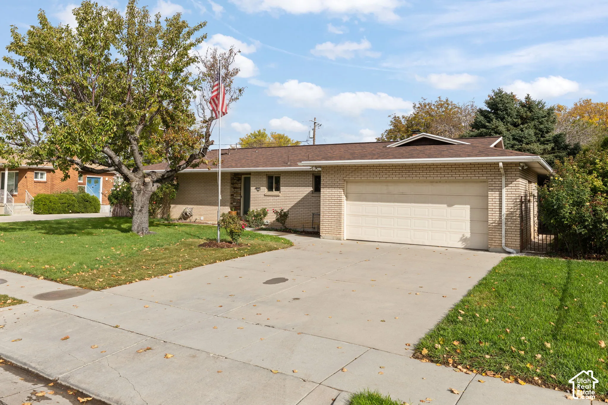 Single-story brick exterior featuring a multi-pitched shingled roof, attached two-car garage, concrete driveway, and mature landscaping