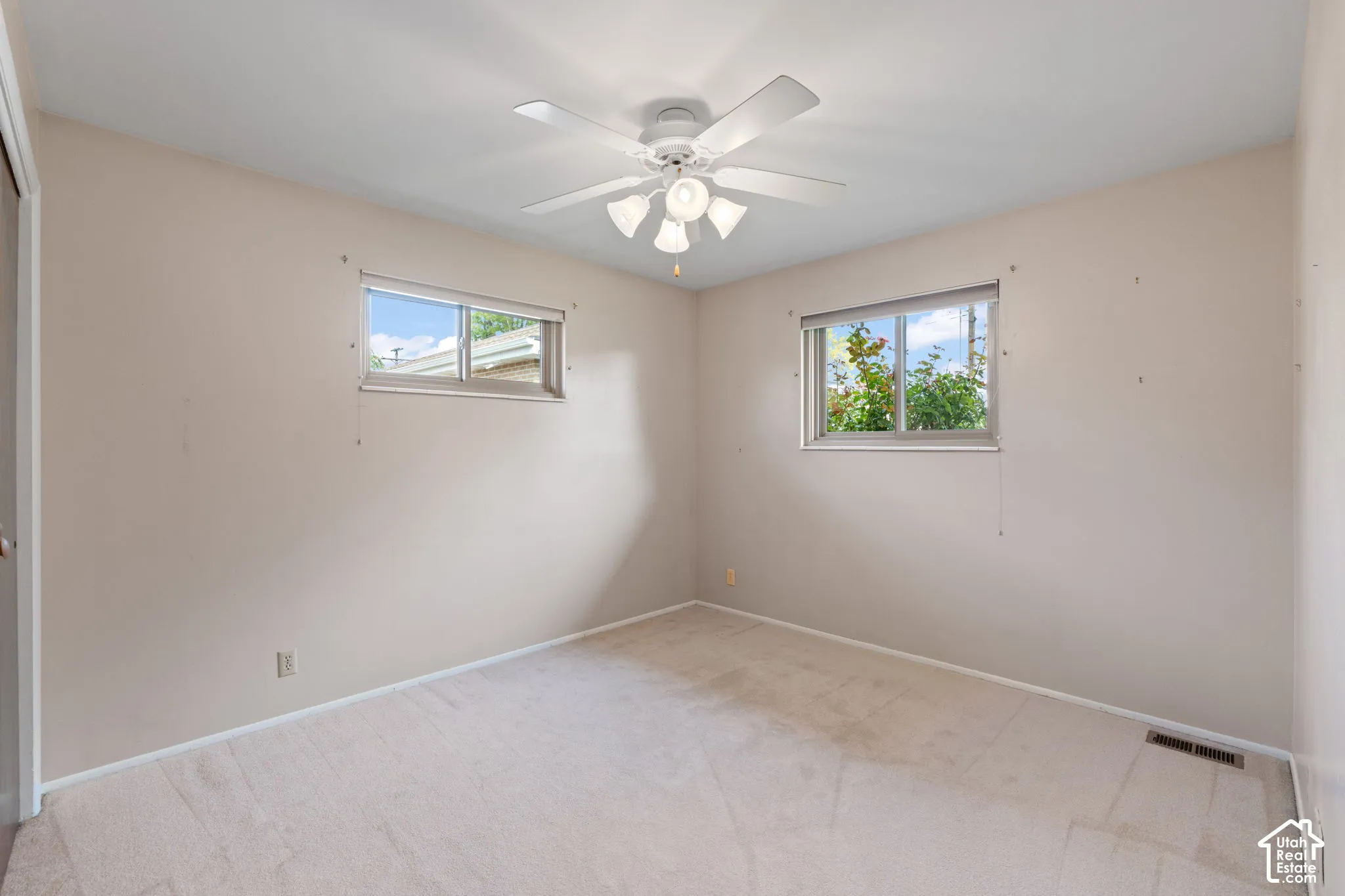 Neutral-toned interior featuring dual sliding windows, neutral carpeting, and a ceiling-mounted light fixture with a multi-blade fan