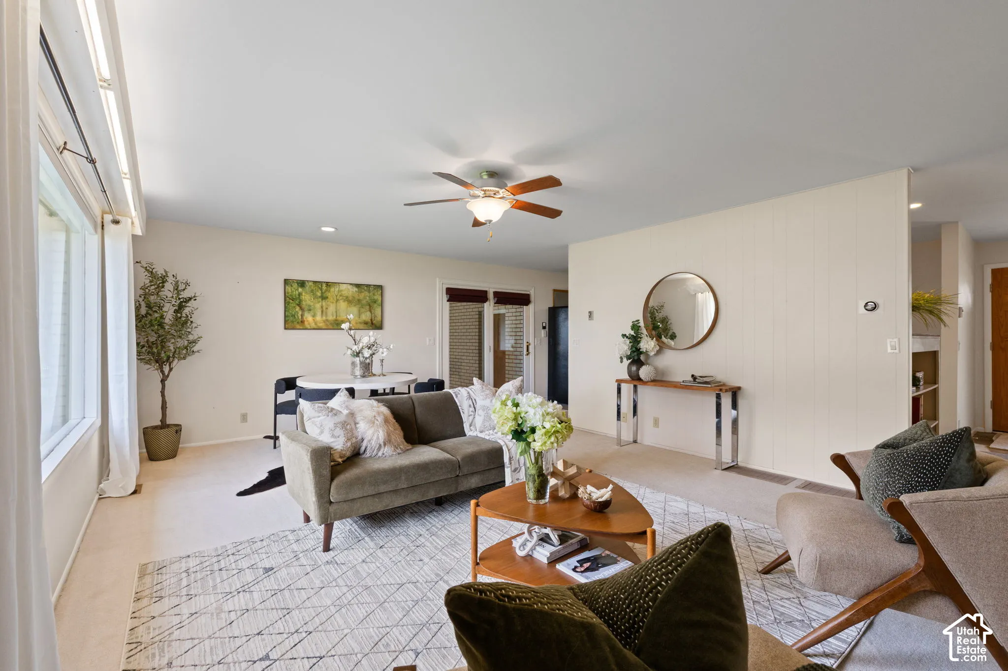 Neutral-toned living space featuring a ceiling fan with integrated lighting, oversized windows, and wall-paneling detail