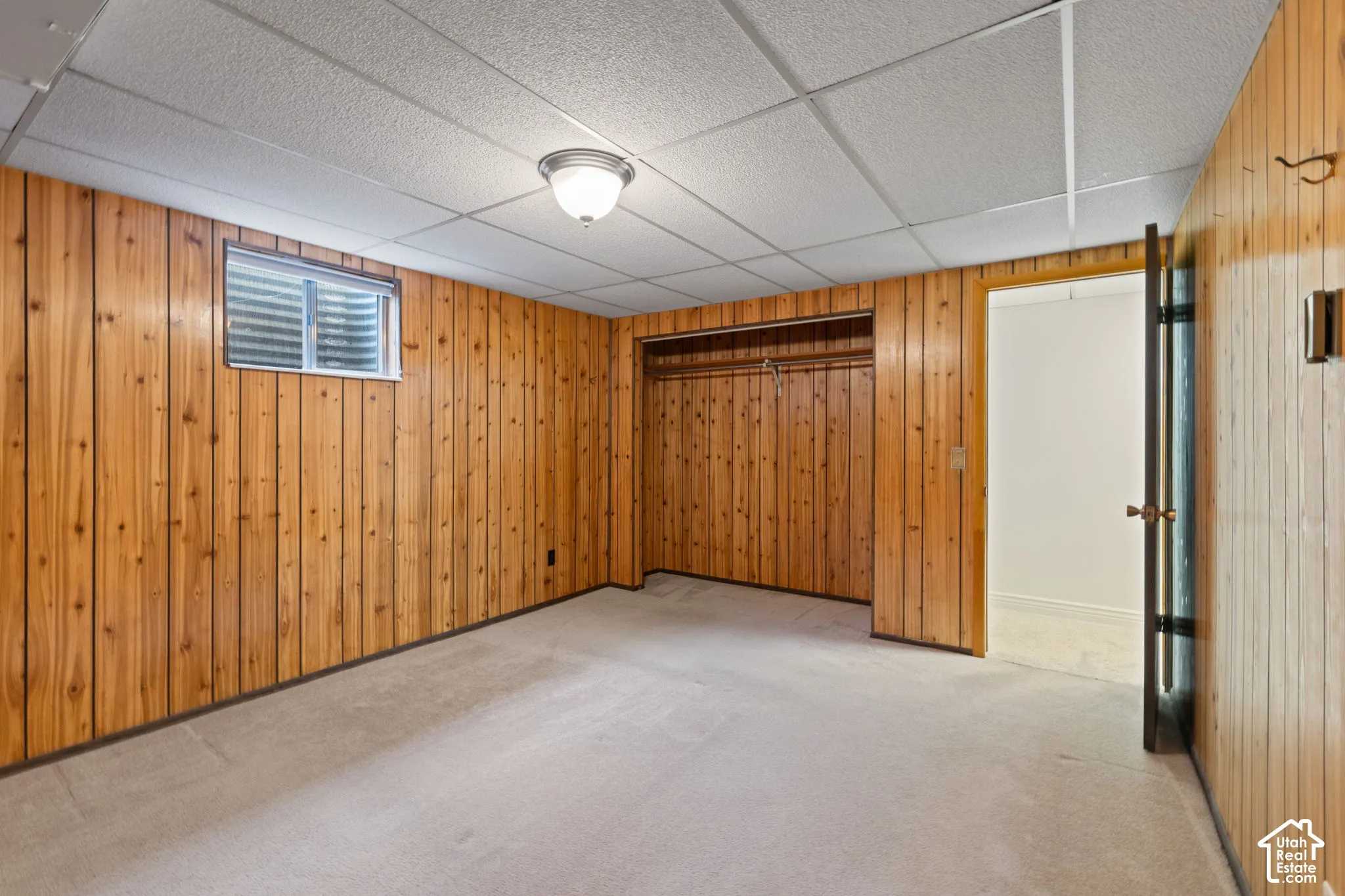Wood-paneled wall finishes, carpeted flooring, drop ceiling with flush-mount lighting, and built-in closet space
