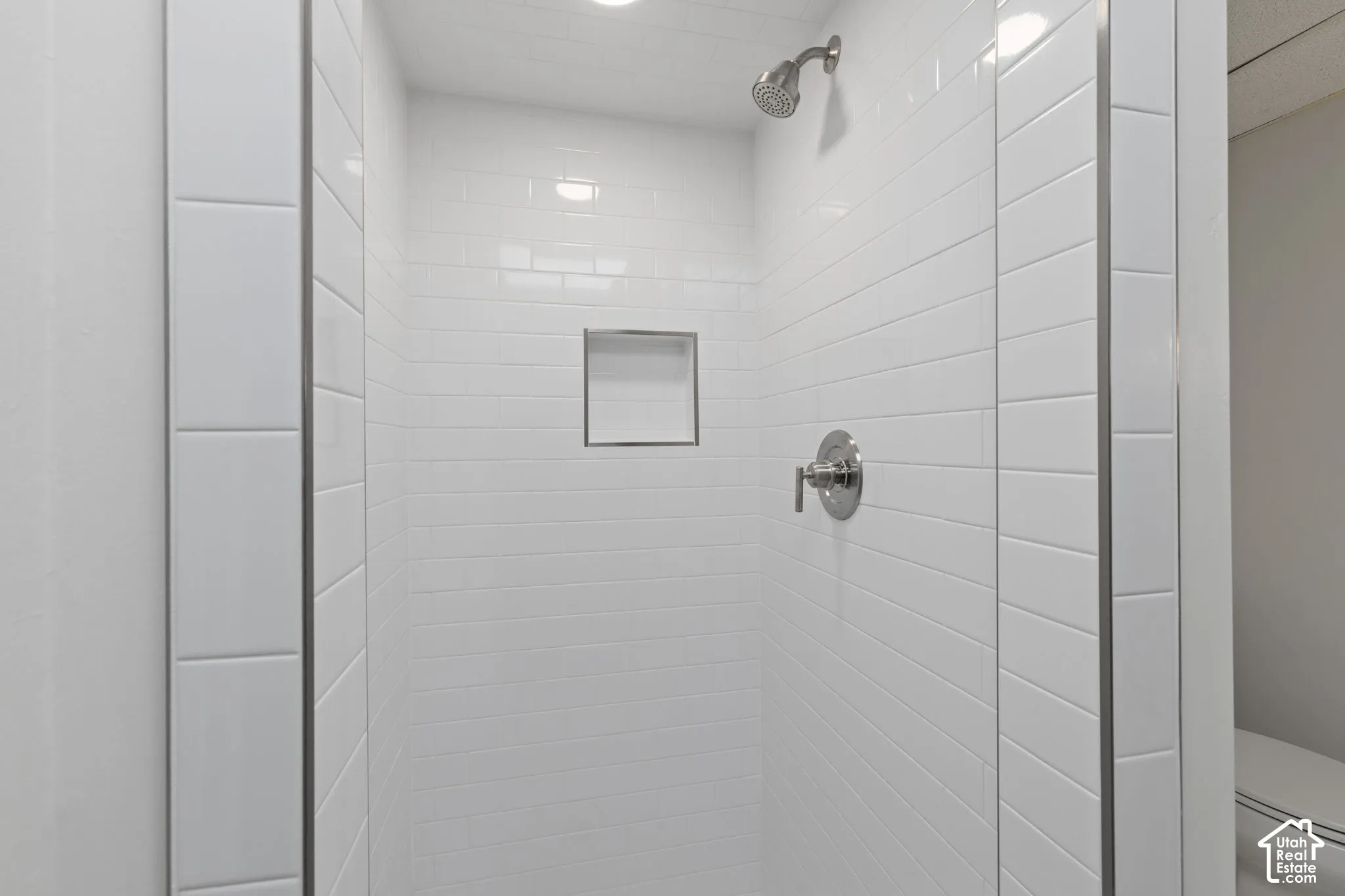 Shower enclosure featuring white subway tile walls, a built-in tiled niche, and polished chrome fixtures