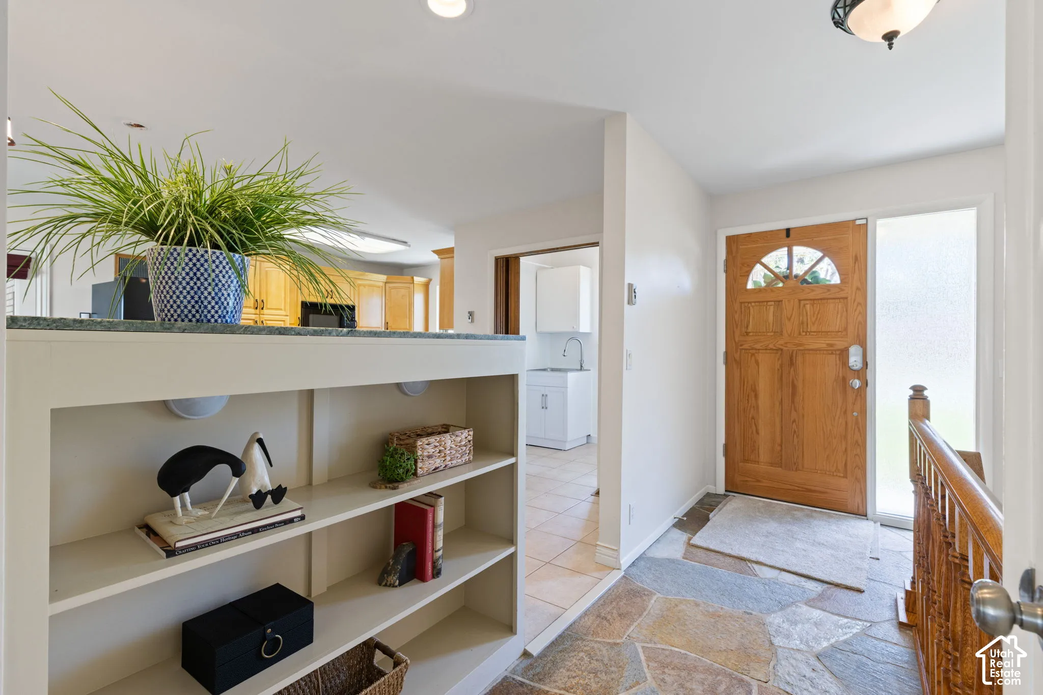 Entryway featuring natural stone flooring, a solid wood front door with a half-moon glass insert, integrated shelving with a stone surface, and a wooden staircase balustrade