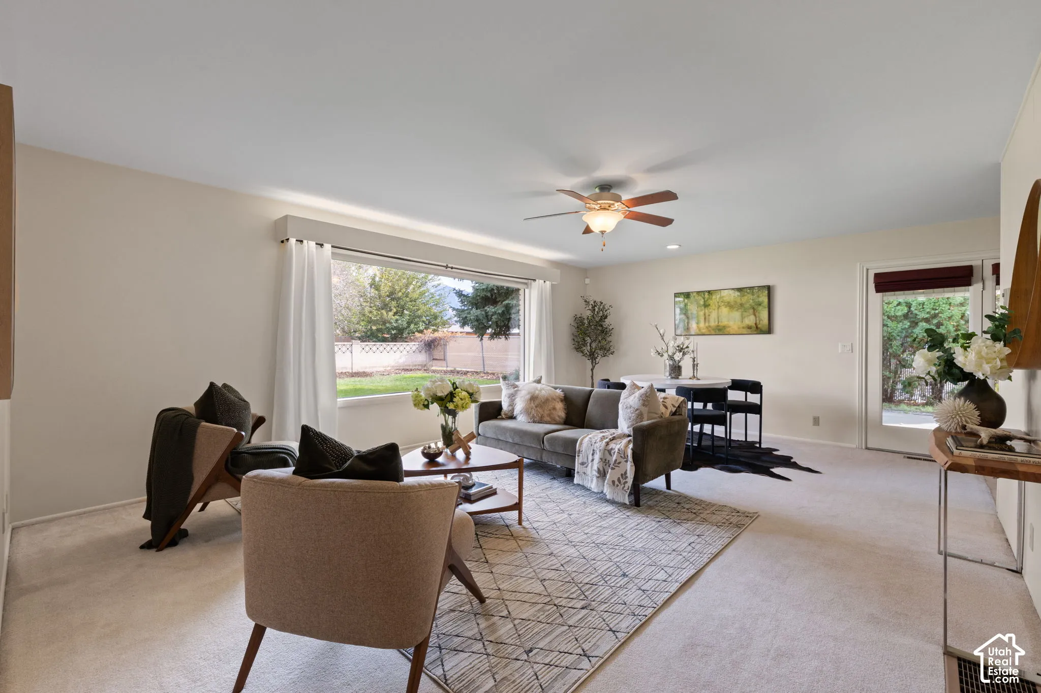 Open-concept interior space featuring neutral wall tones, carpeted flooring, a ceiling fan with integrated lighting, a large picture window, and a glass-paneled exterior door