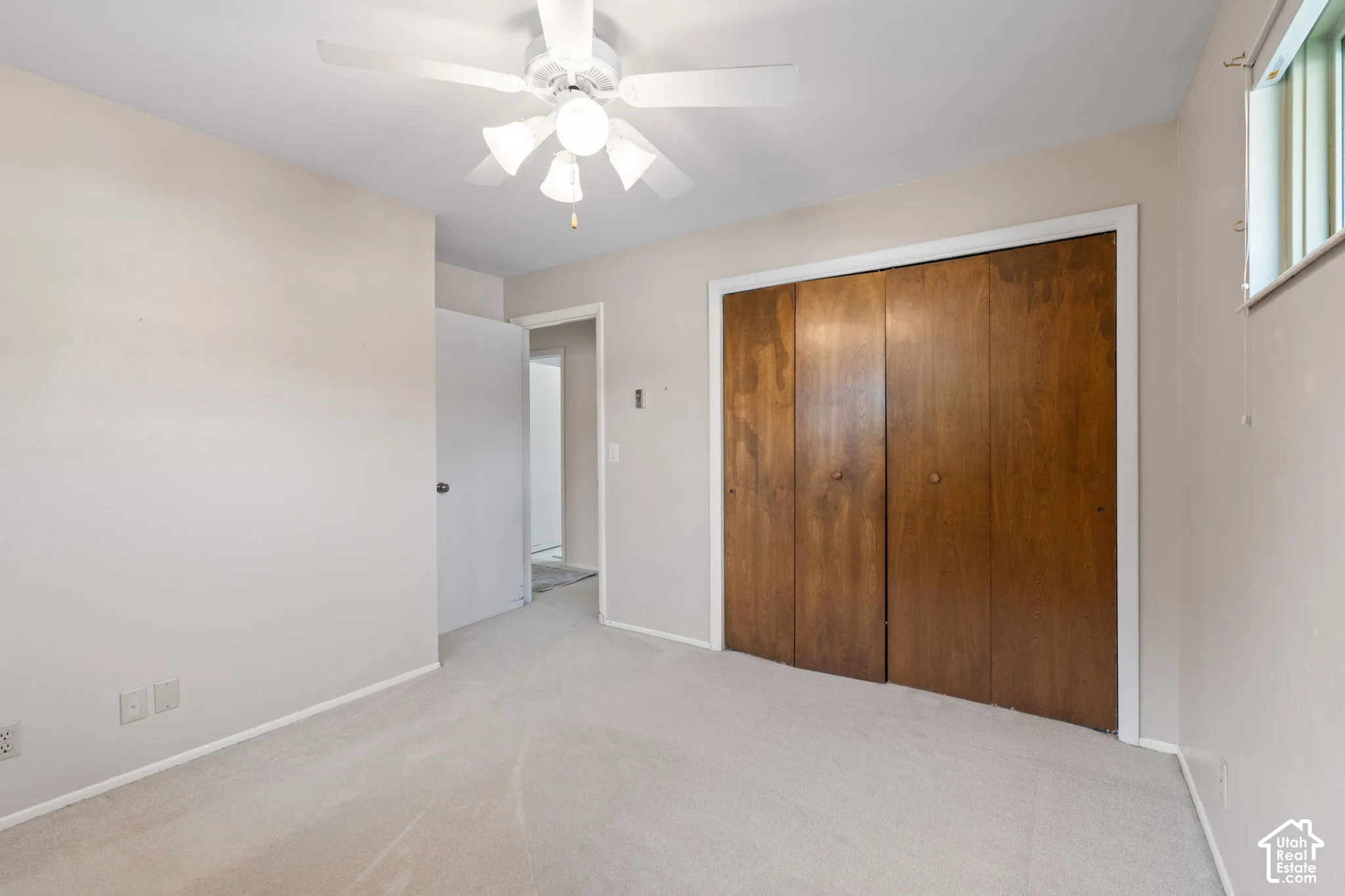 Neutral interior featuring a ceiling fan with integrated light fixture, carpeted flooring, and a sliding closet with wood-finish doors