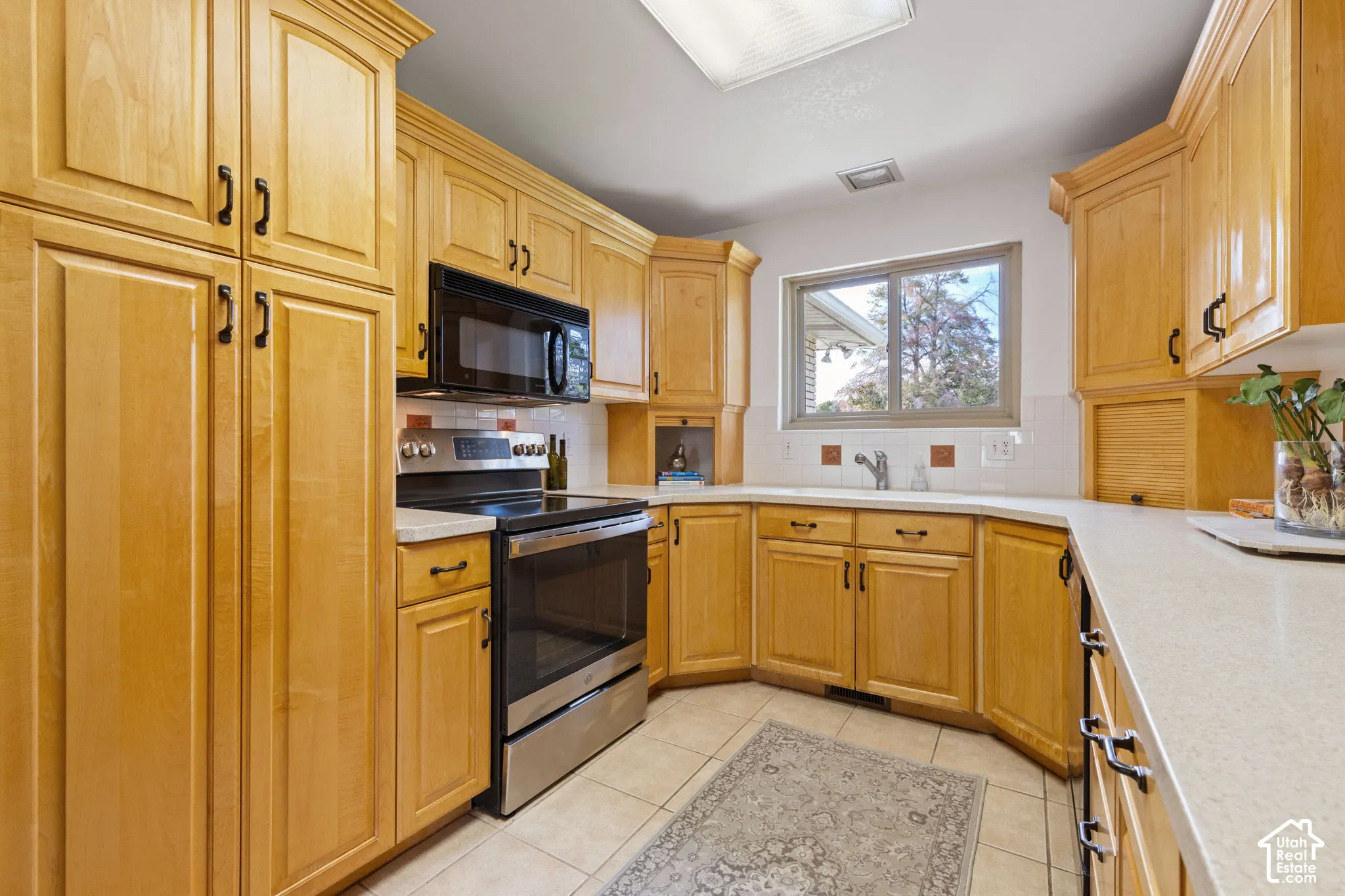 Kitchen featuring light-finish cabinetry, solid surface countertops, stainless steel appliances, and ceramic tile flooring