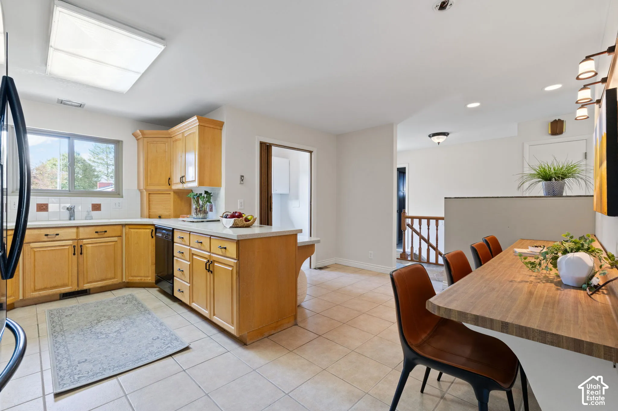 Kitchen featuring natural wood cabinetry, solid surface countertops, tile flooring, built-in dishwasher, and a peninsula breakfast bar