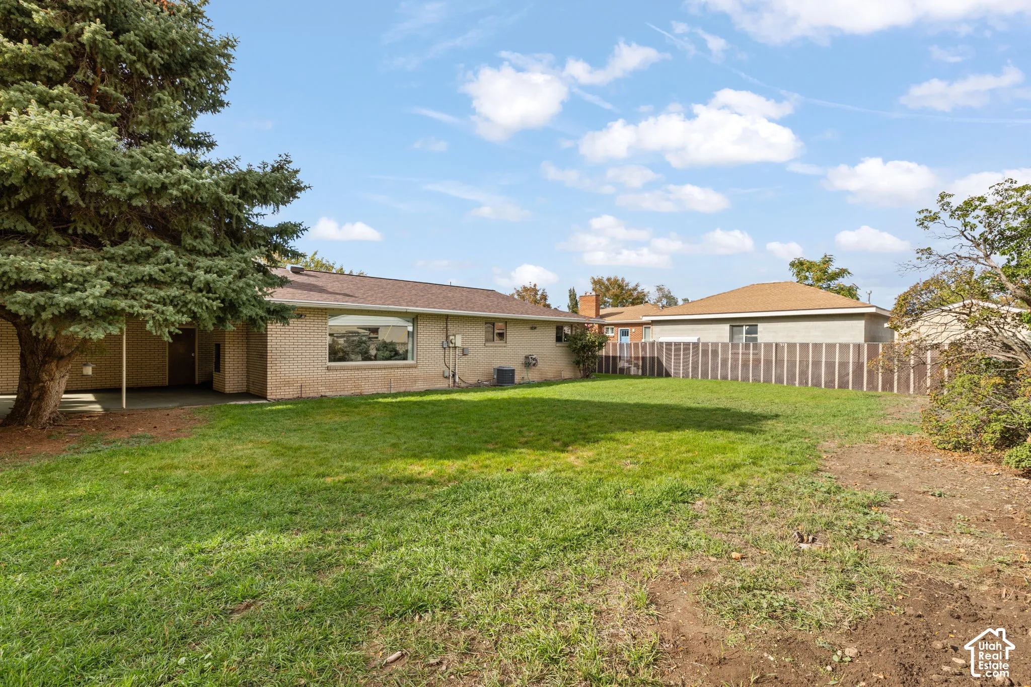 Expansive backyard featuring a brick exterior, covered patio, mature evergreen tree, and wood-style privacy fencing