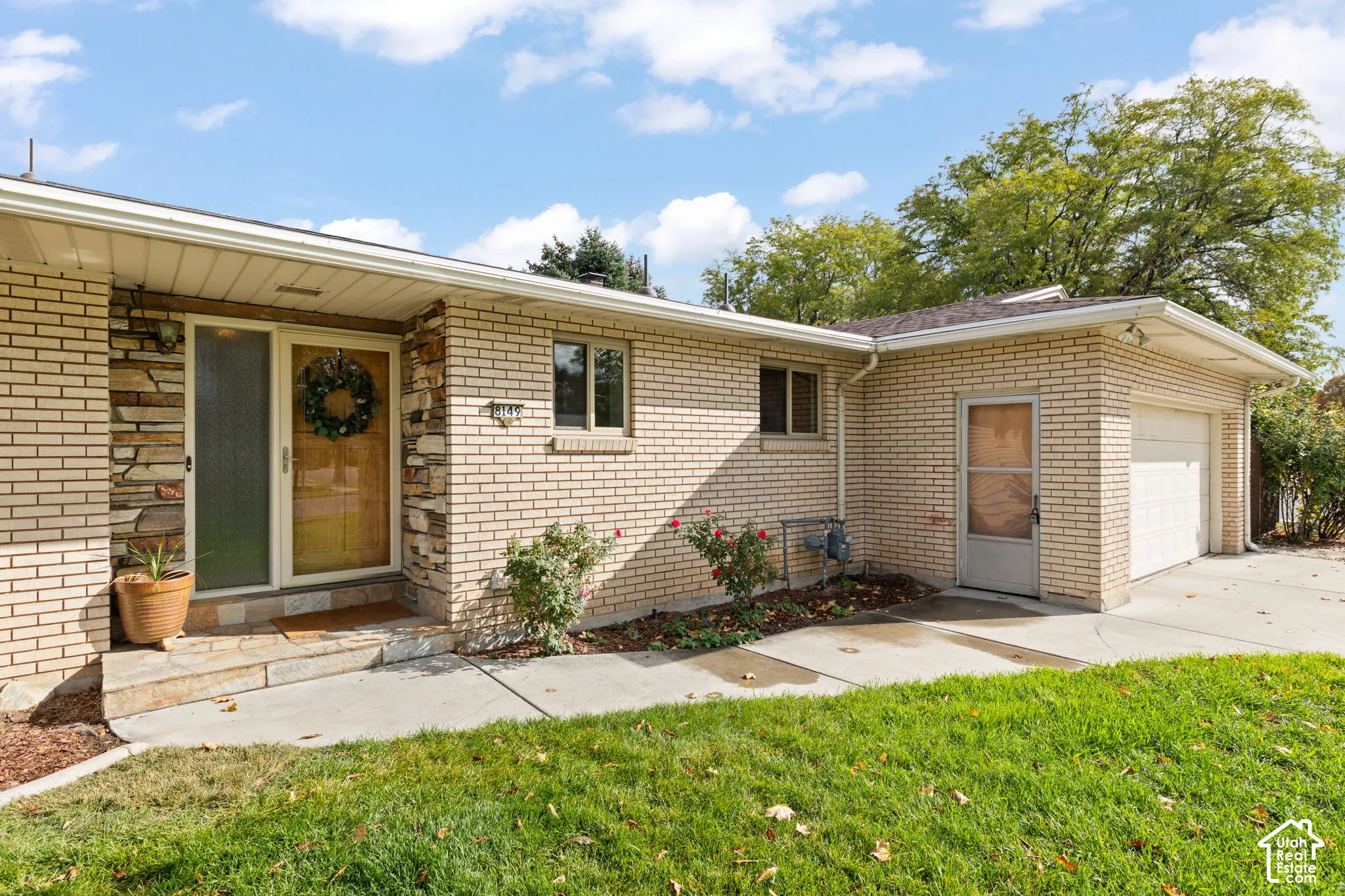 Single-story brick exterior featuring a stone-accented entryway, covered porch, attached garage, and concrete walkway