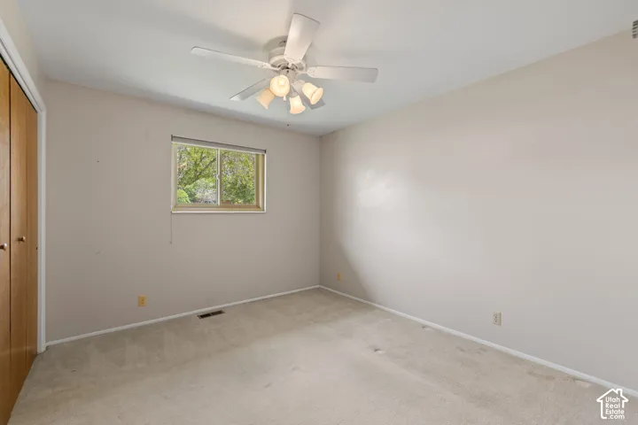 Neutral-toned interior space featuring wall-to-wall carpeting, a multi-light ceiling fan, and double-door closet cabinetry