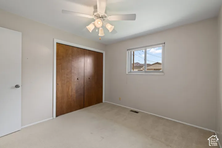 Room featuring neutral carpeting, a ceiling-mounted light fixture with a fan, a sliding closet with wood-finish doors, and a single-pane window