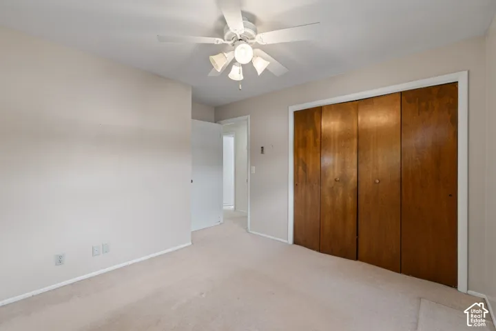 Room featuring wall-to-wall carpeting, wood-finish closet doors, and a ceiling fan with integrated light fixture