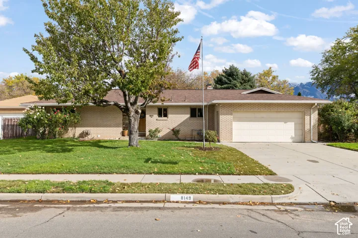 Single-story brick exterior featuring a low-slope roof, attached two-car garage, concrete driveway, and mature landscaping