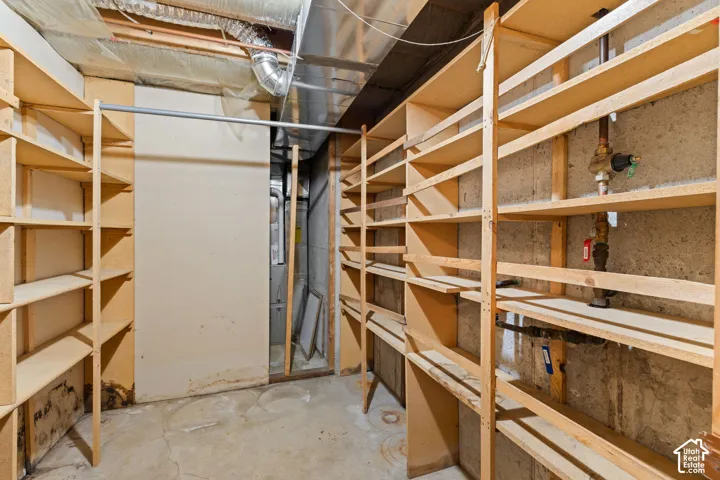 Utility space featuring expansive wood shelving units, exposed concrete foundation walls, and metal ductwork