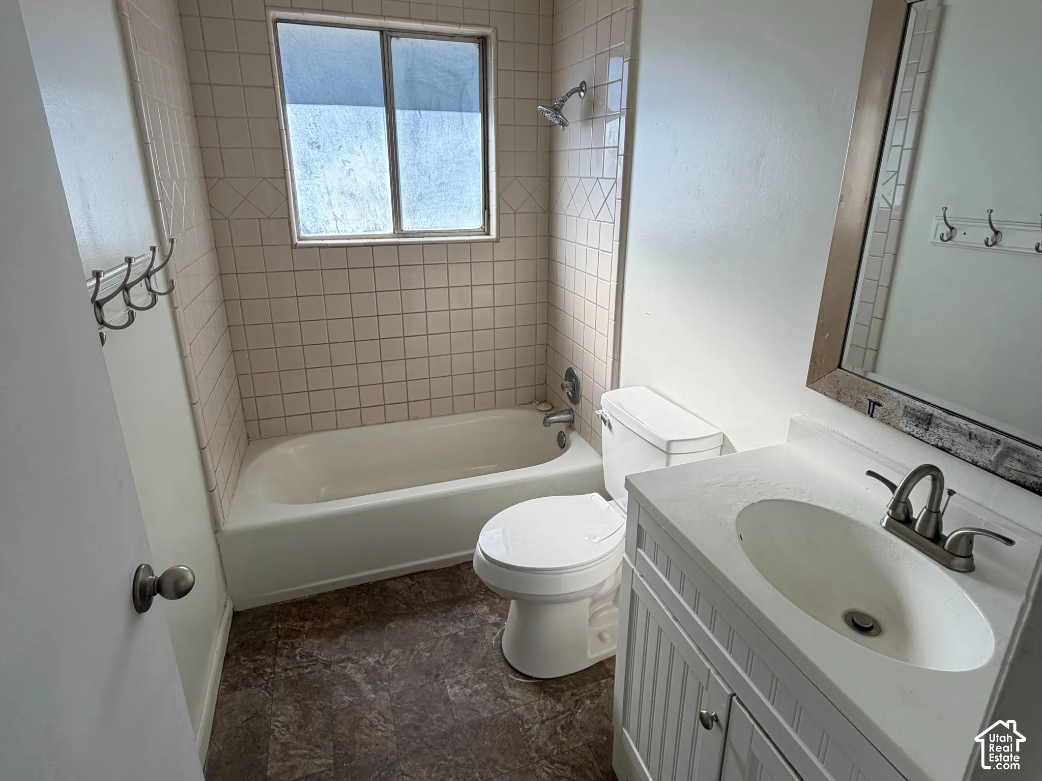 Bathroom featuring a vanity with an integrated basin, tile-surround bathtub, window with privacy glass, wall-mounted light fixture, and stone-pattern flooring
