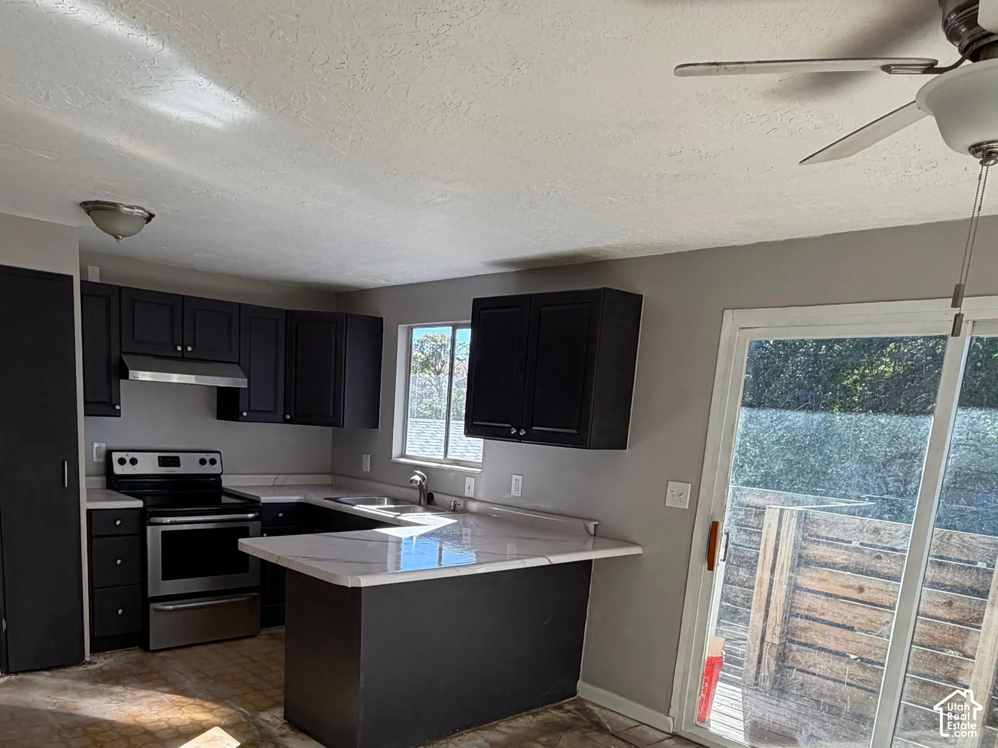 Kitchen featuring dark cabinetry, stone-finish countertops, stainless steel range with integrated hood, and sliding glass door