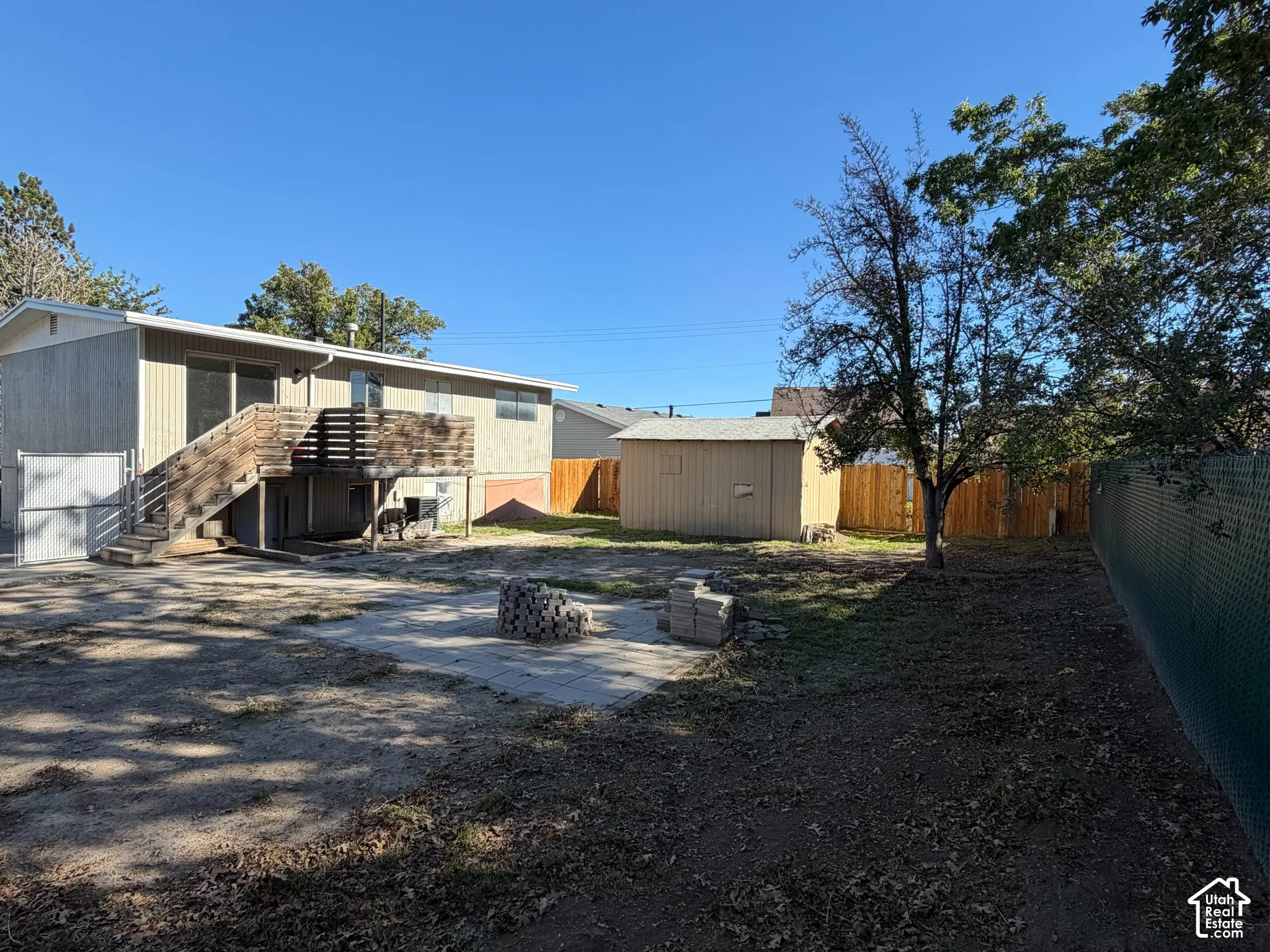 Backyard featuring an elevated wood deck, detached storage shed, stone patio, and perimeter fencing