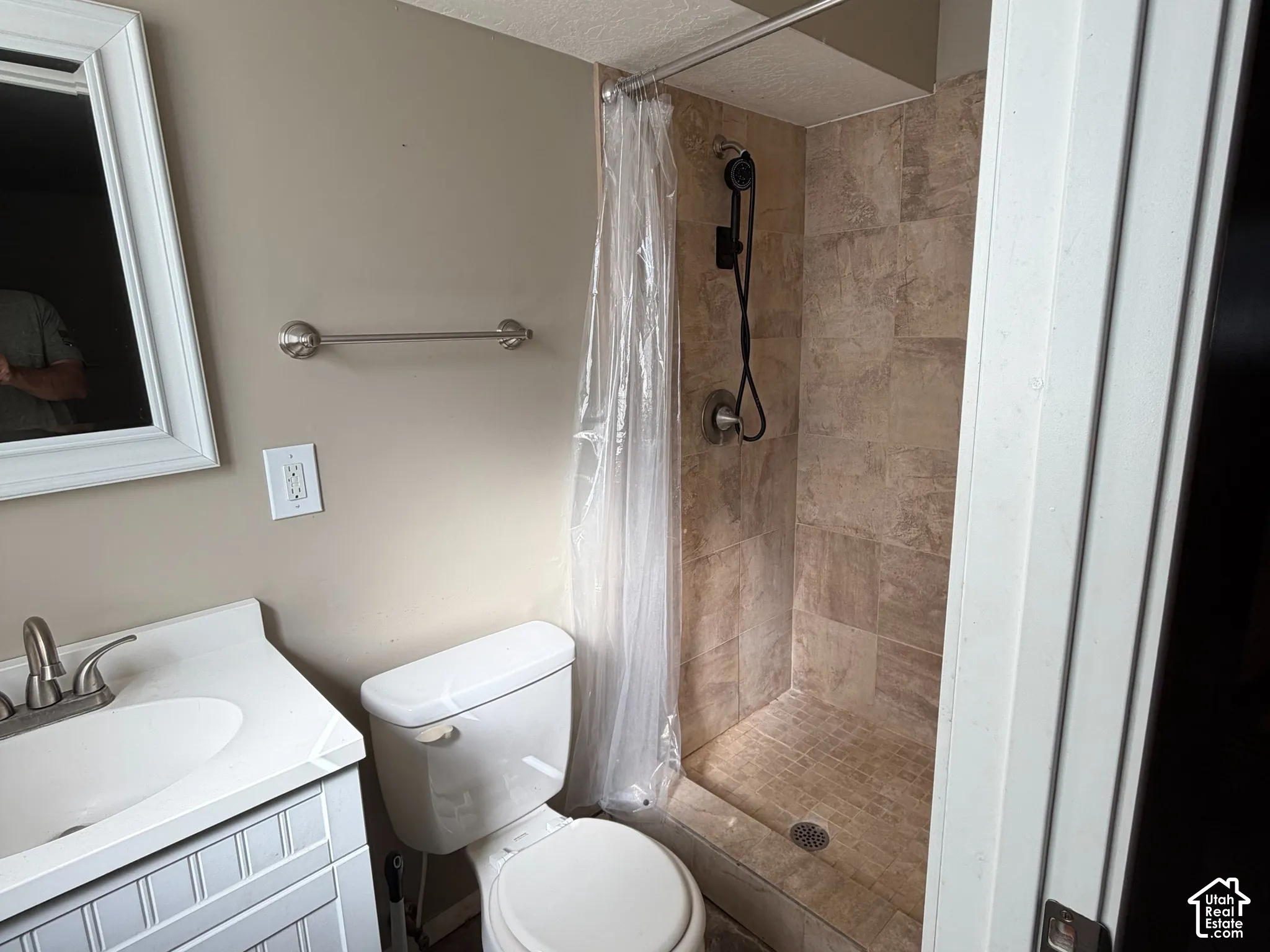 Bathroom featuring a white beadboard vanity, undermount sink, ceramic tile shower surround, shower pan with tile flooring, and a handheld shower fixture